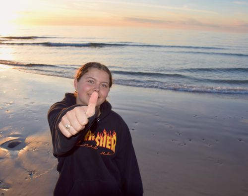 Kristen efterskole i Jylland. En pige fra Sædding Efterskole står på stranden med en solnedgang i baggrunden. Hun smiler og giver thumbs up.