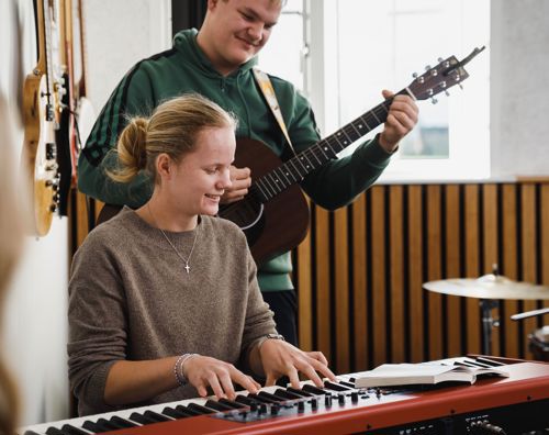 En efterskolepige spille klaver mens en dreng spiller guitar til i musiklokalet på Sædding Efterskole